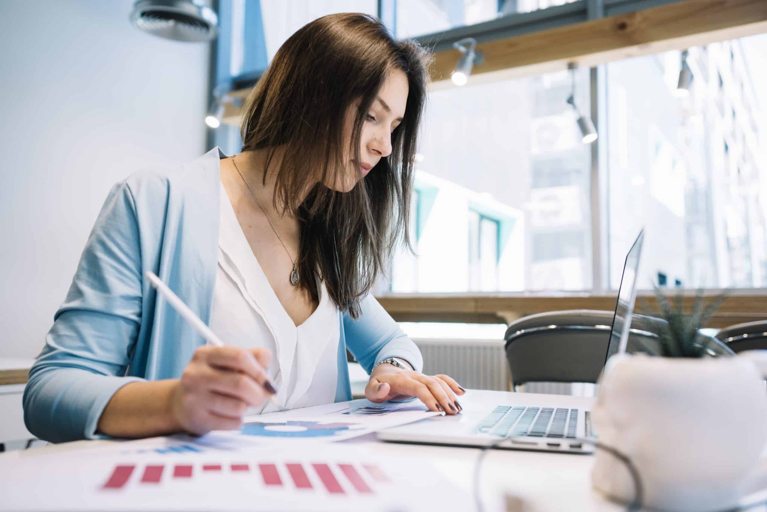 mulher sentada em seu local de trabalho de contabilidade com documentos e um notebook em sua volta.
