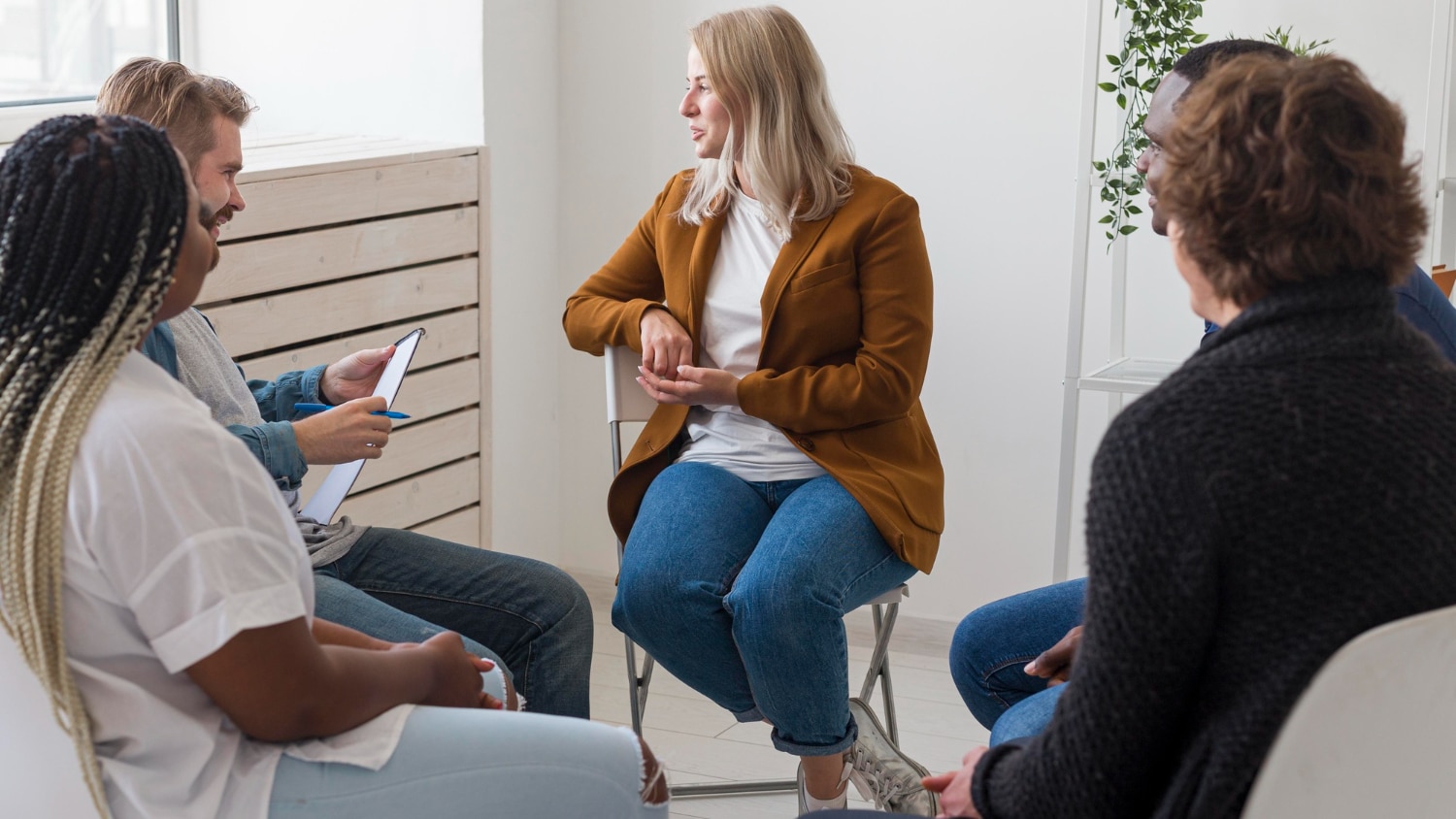 grupo de pessoas sentadas em uma roda conversando. Enquanto uma mulher fala outra pessoa segura uma prancheta para anotações.
