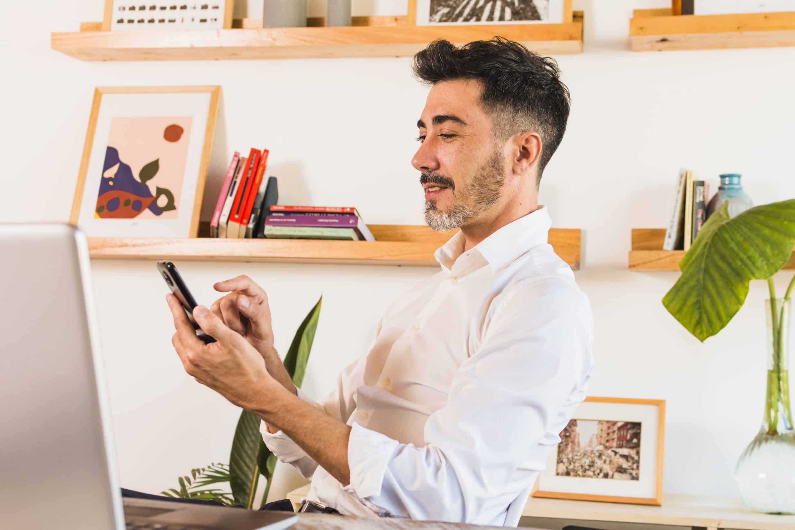 homem sentado em local de trabalho ou estudos segurando o celular