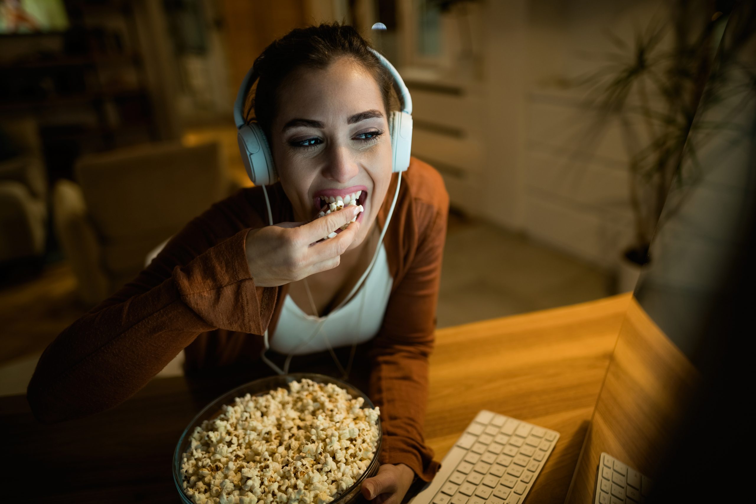 mulher sentada em frente ao computador comendo pipoca e assistindo séries