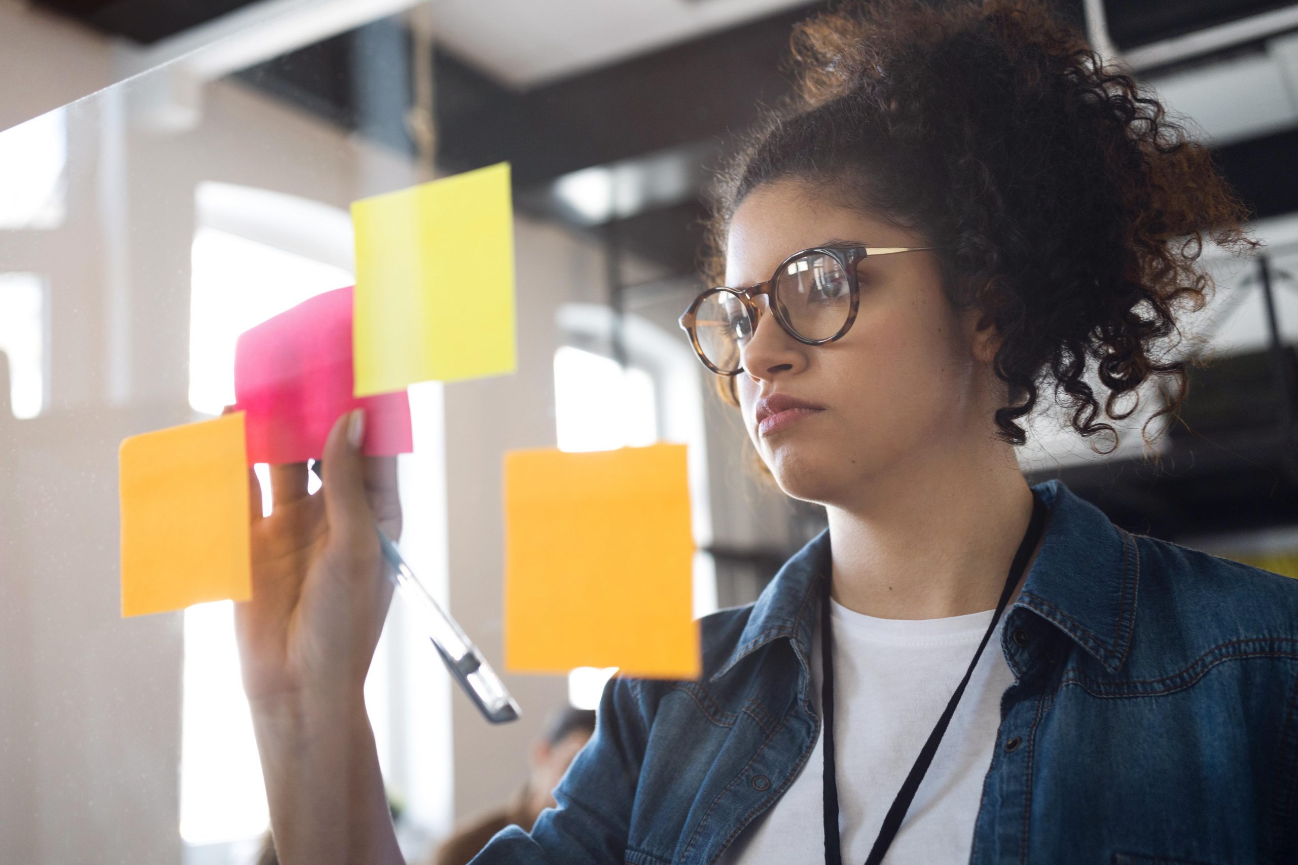 menina em pé de frente para um vidro escrevendo em postit colorido
