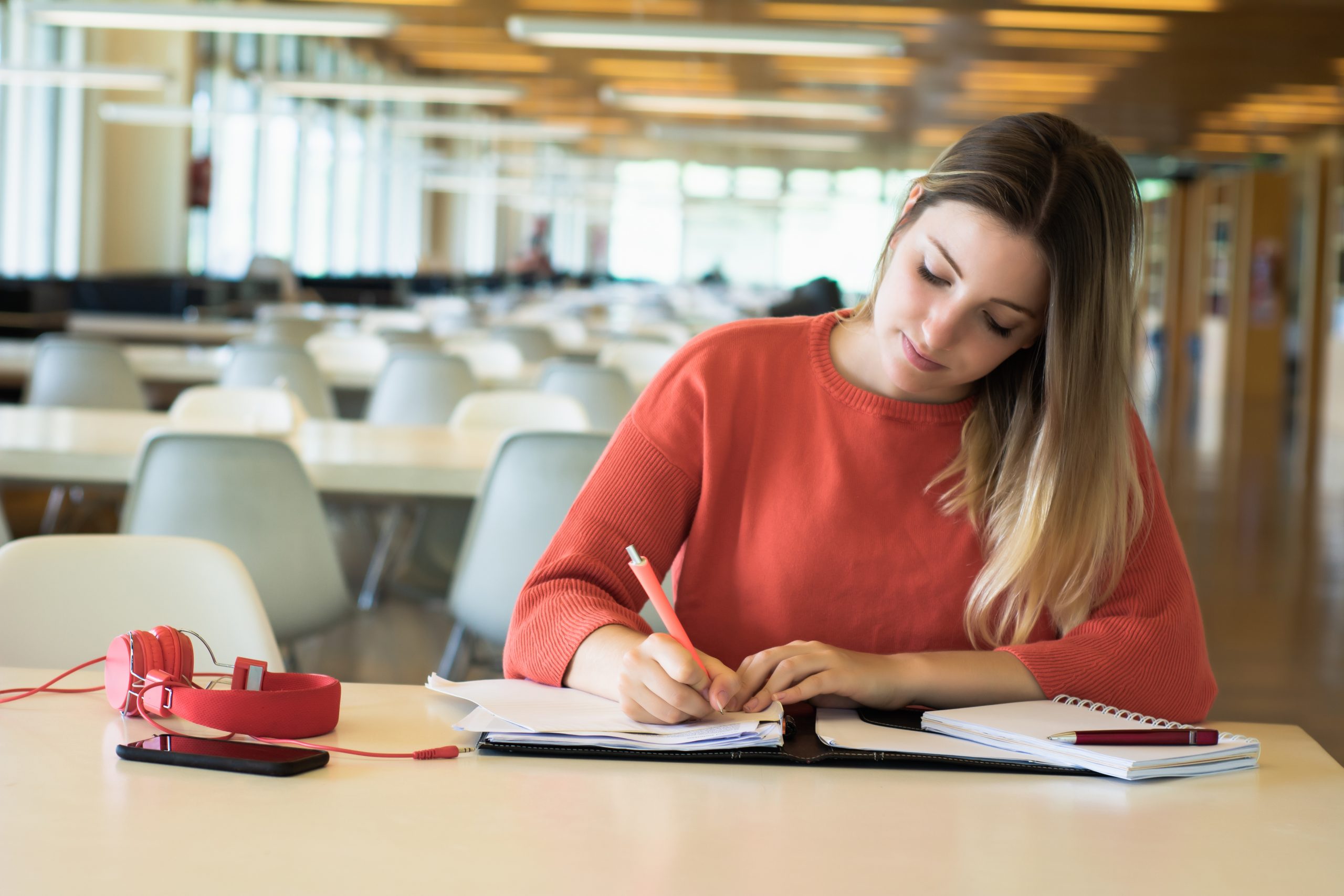 mulher escrevendo em um caderno. Ela está em um ambiente escolar
