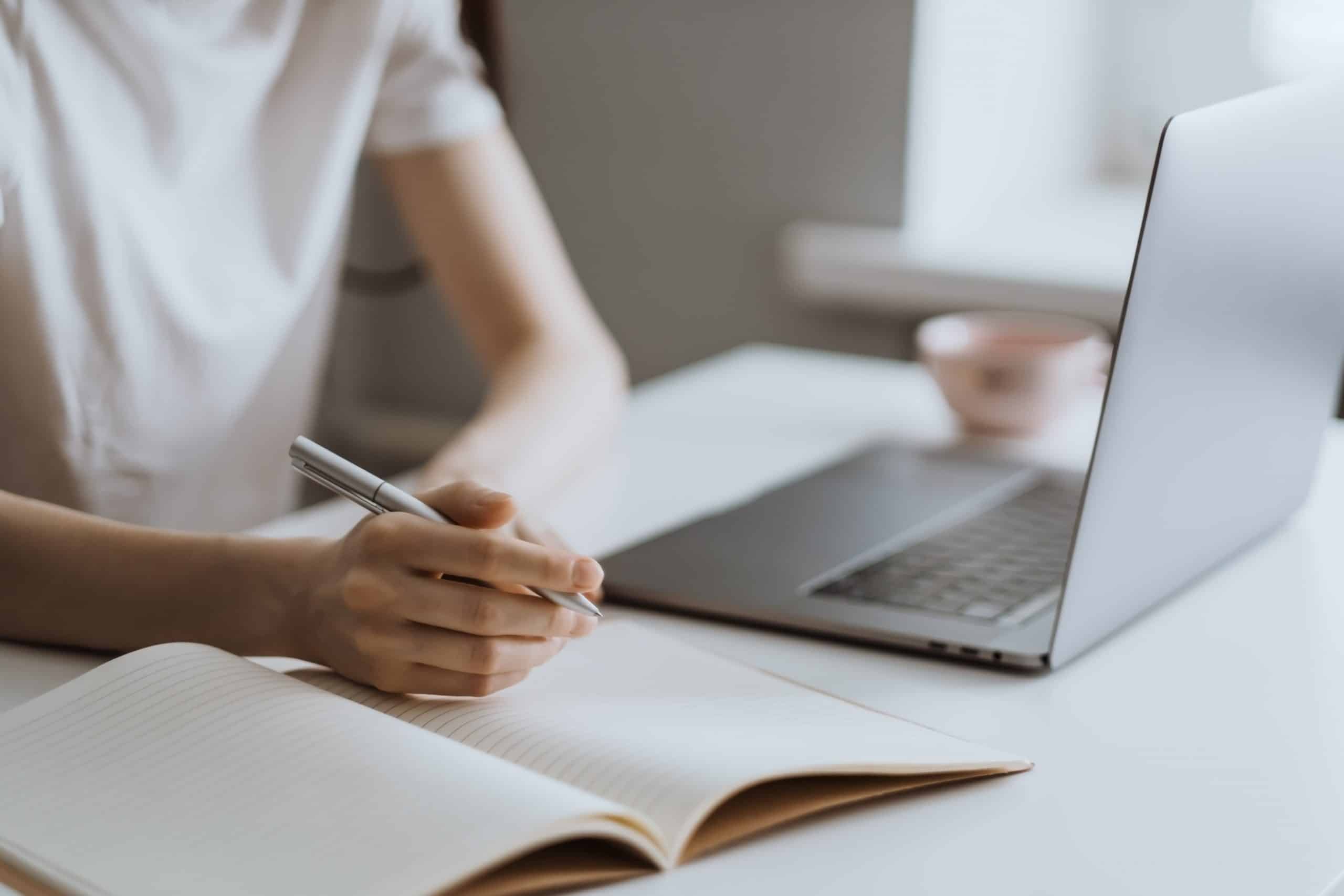 uma pessoa com notebook e um caderno ao lado fazendo anotações de estudos