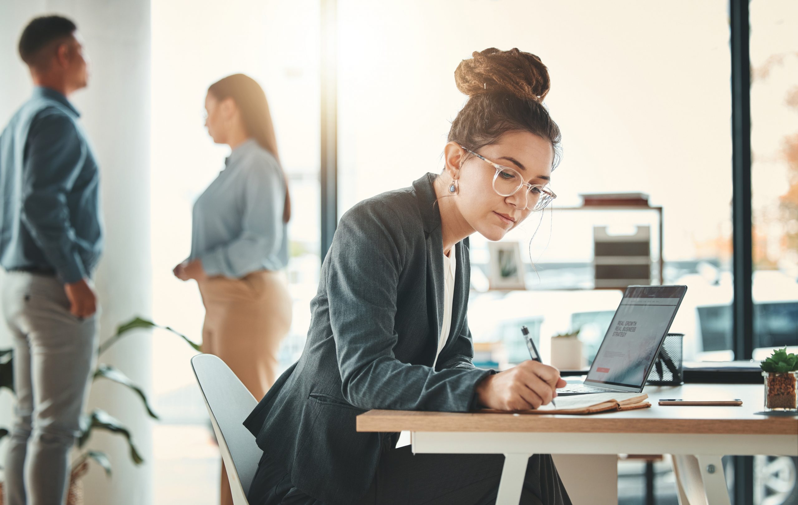 uma mulher em ambiente de trabalho. com computador e fazendo anotações em um bloco de papel