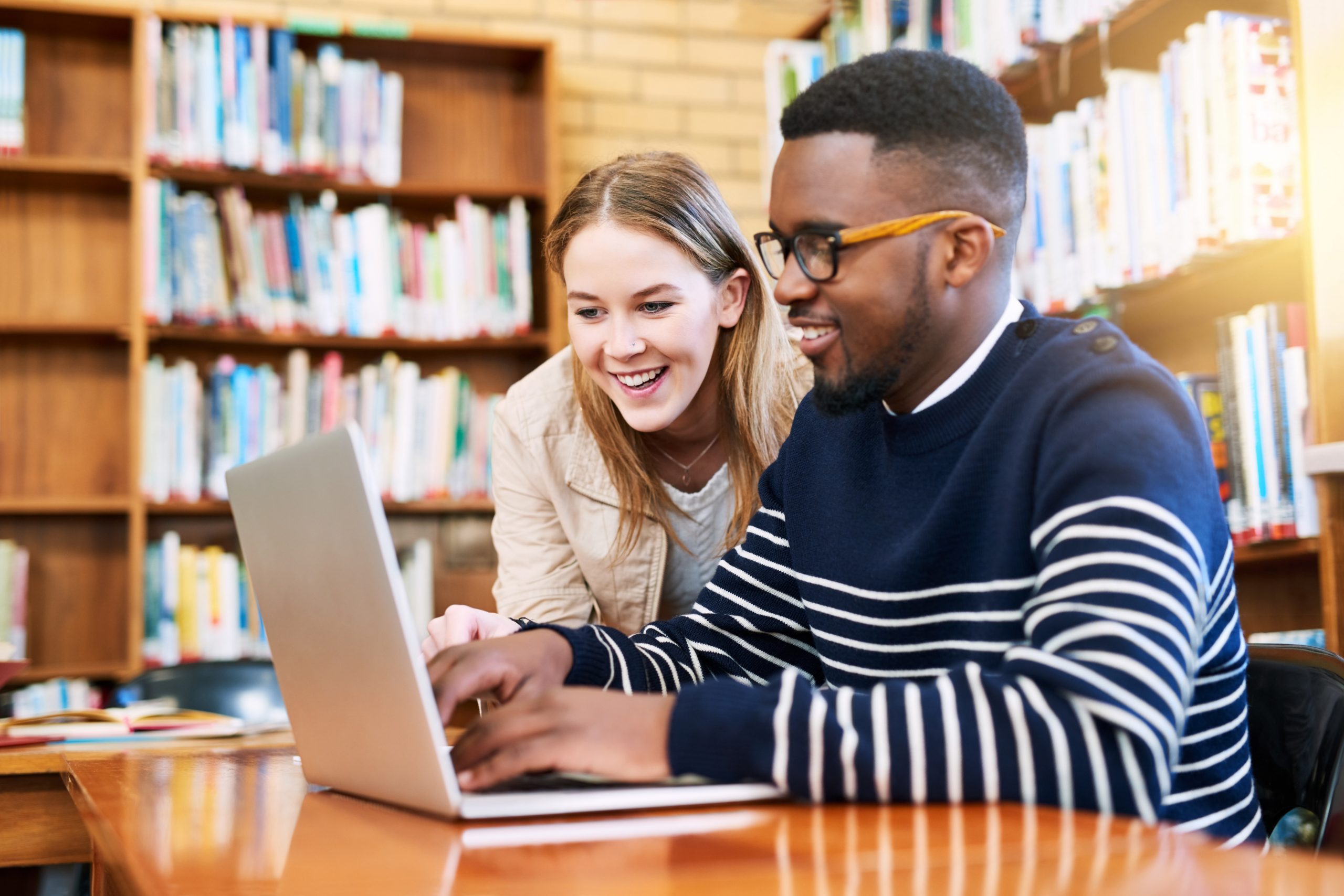 dois colegas em rente ao computador na biblioteca da faculdade