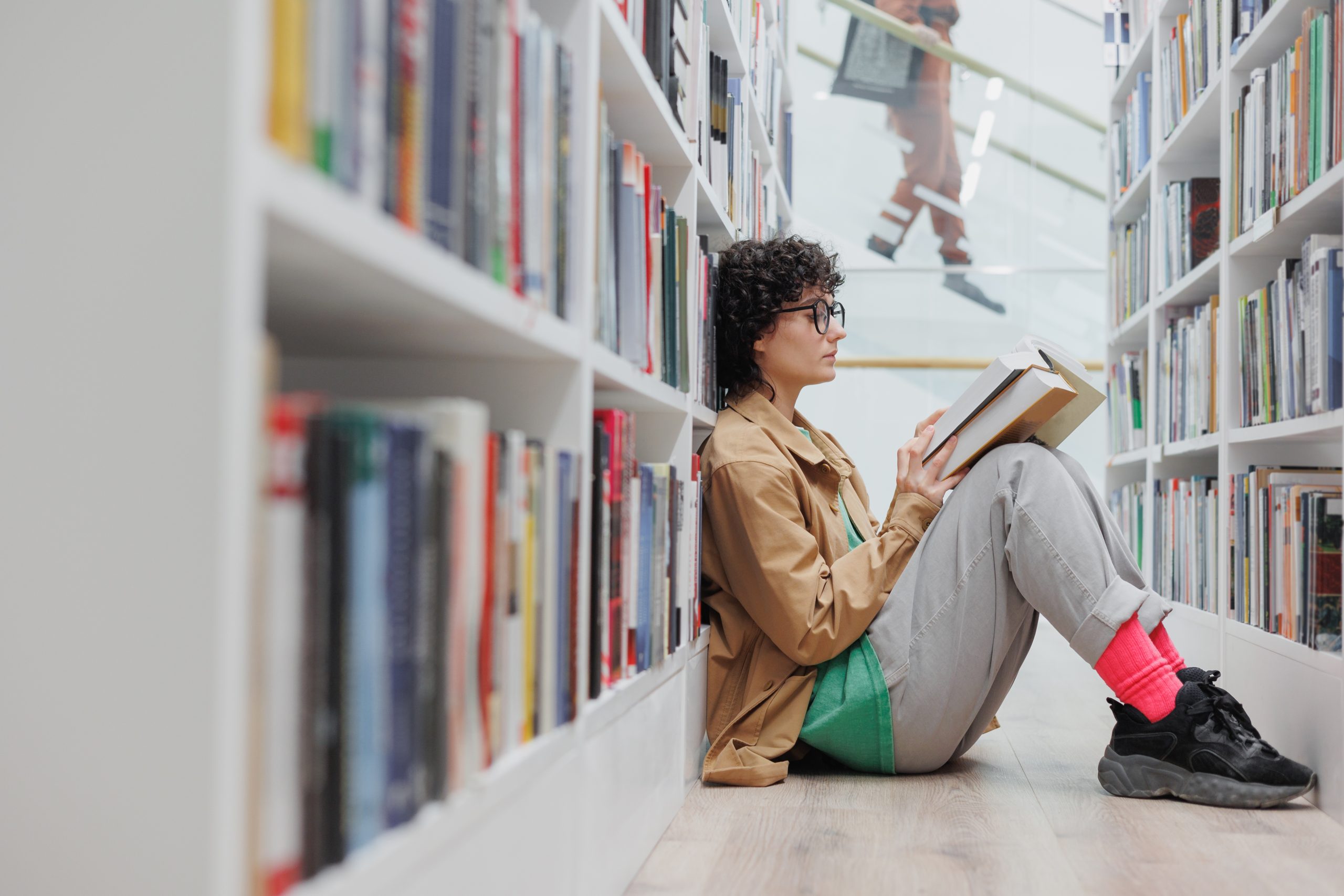 jovem adulta sentada no chão de uma biblioteca lendo