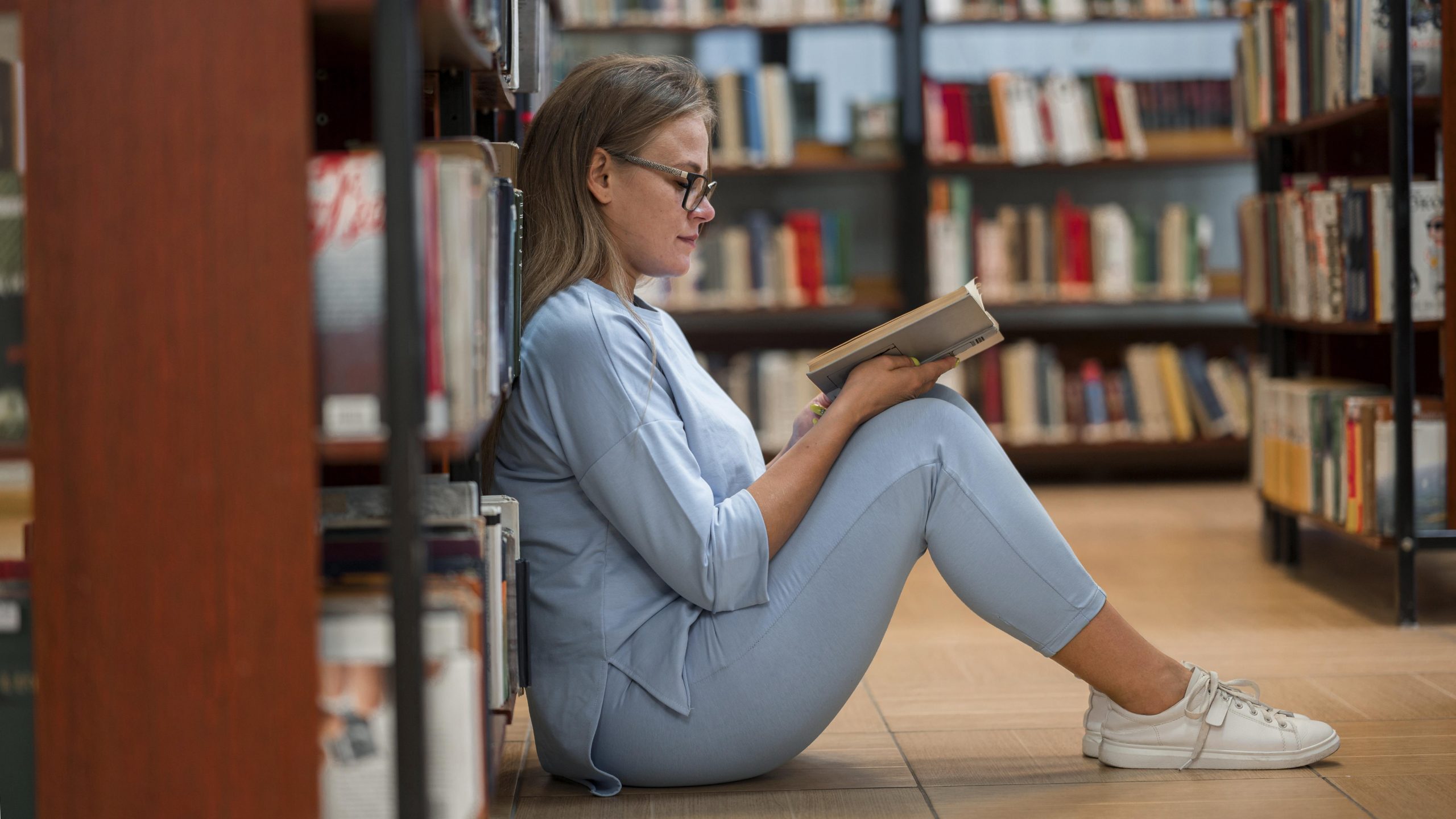 mulher sentada em uma biblioteca lendo um livro
