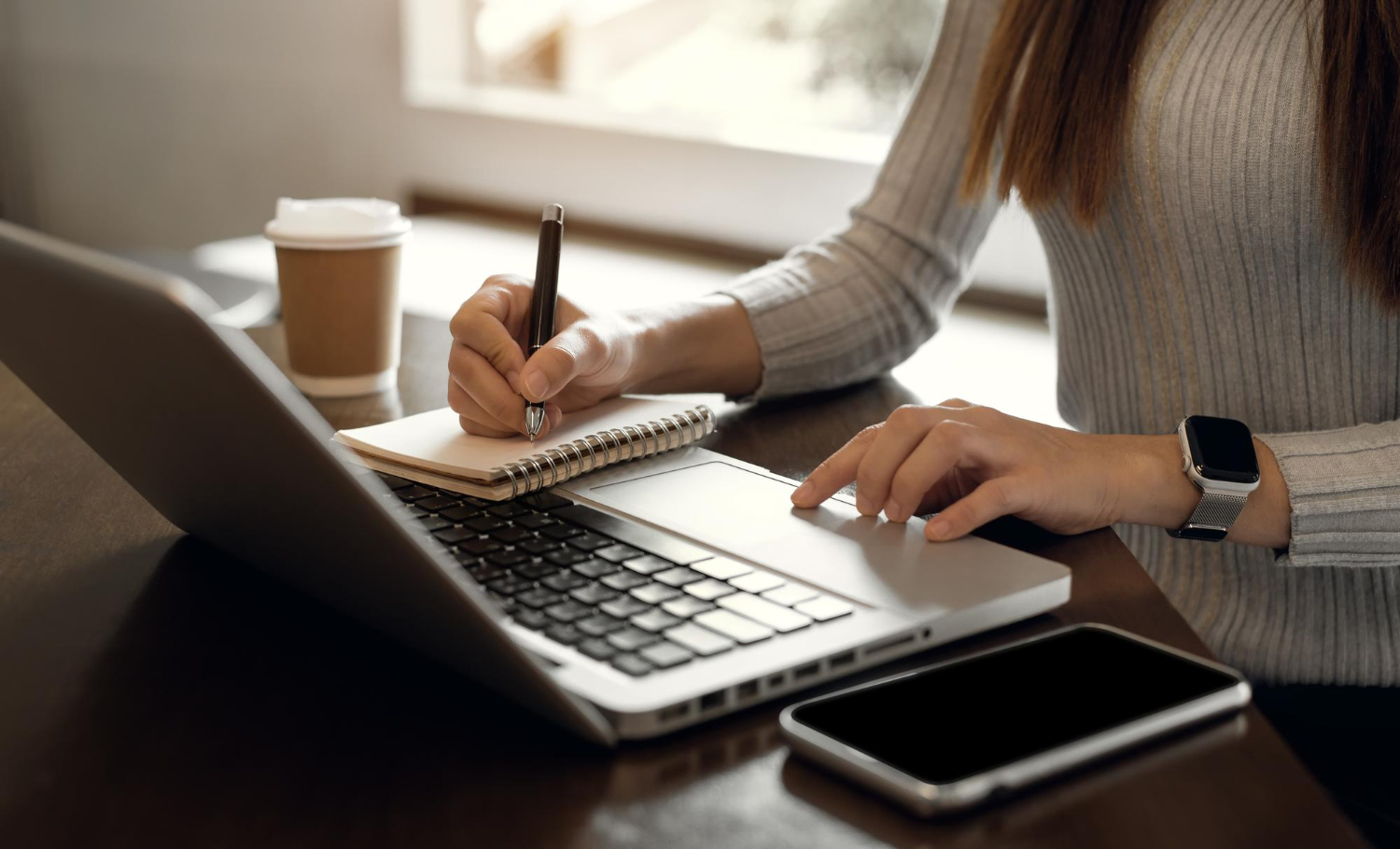 mãos de uma mulher escrevendo em um bloco em cima do notebook