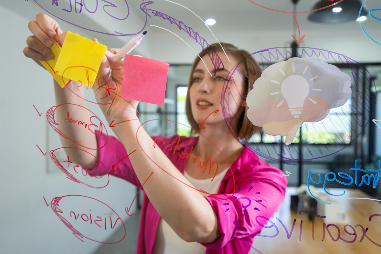 mulher em pé riscando em um vidro com postit, como se tivesse em momento de criatividade