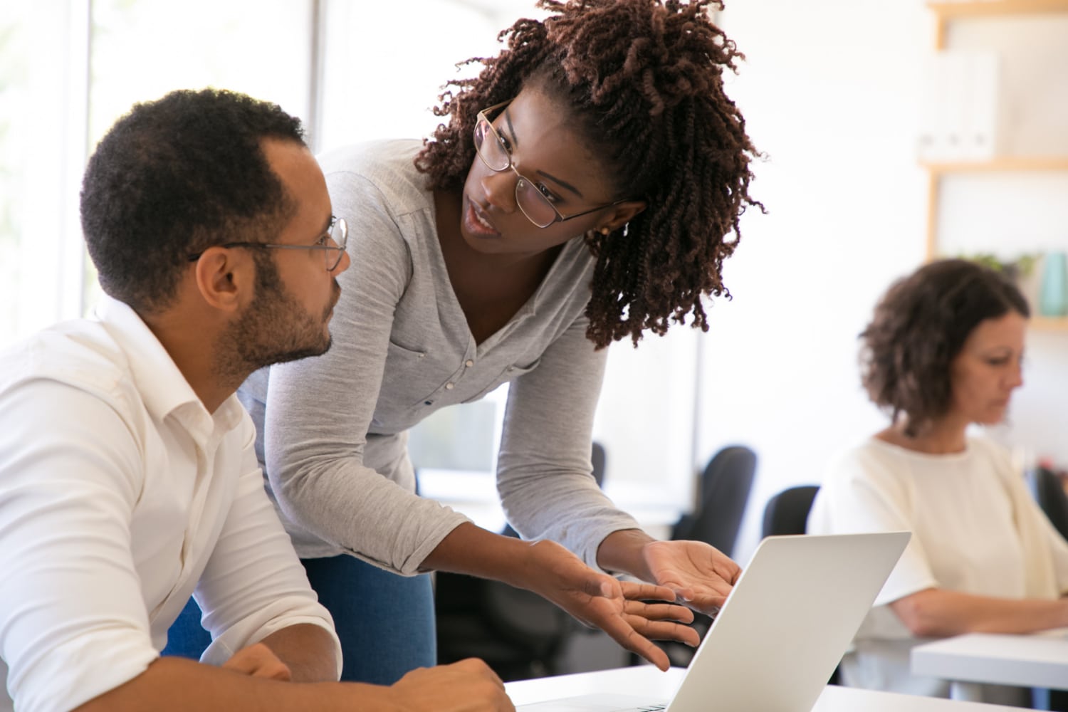 gestora ensinando um jovem trainee que está sentado ao seu lado de frente para notebook