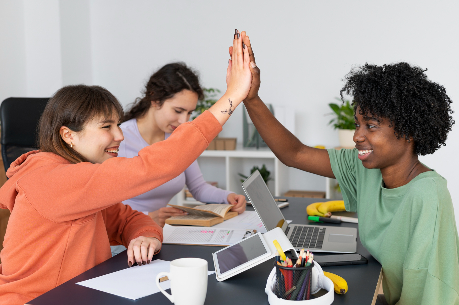 grupo de pessoas sentadas em volta de uma mesa de trabalho comemorando