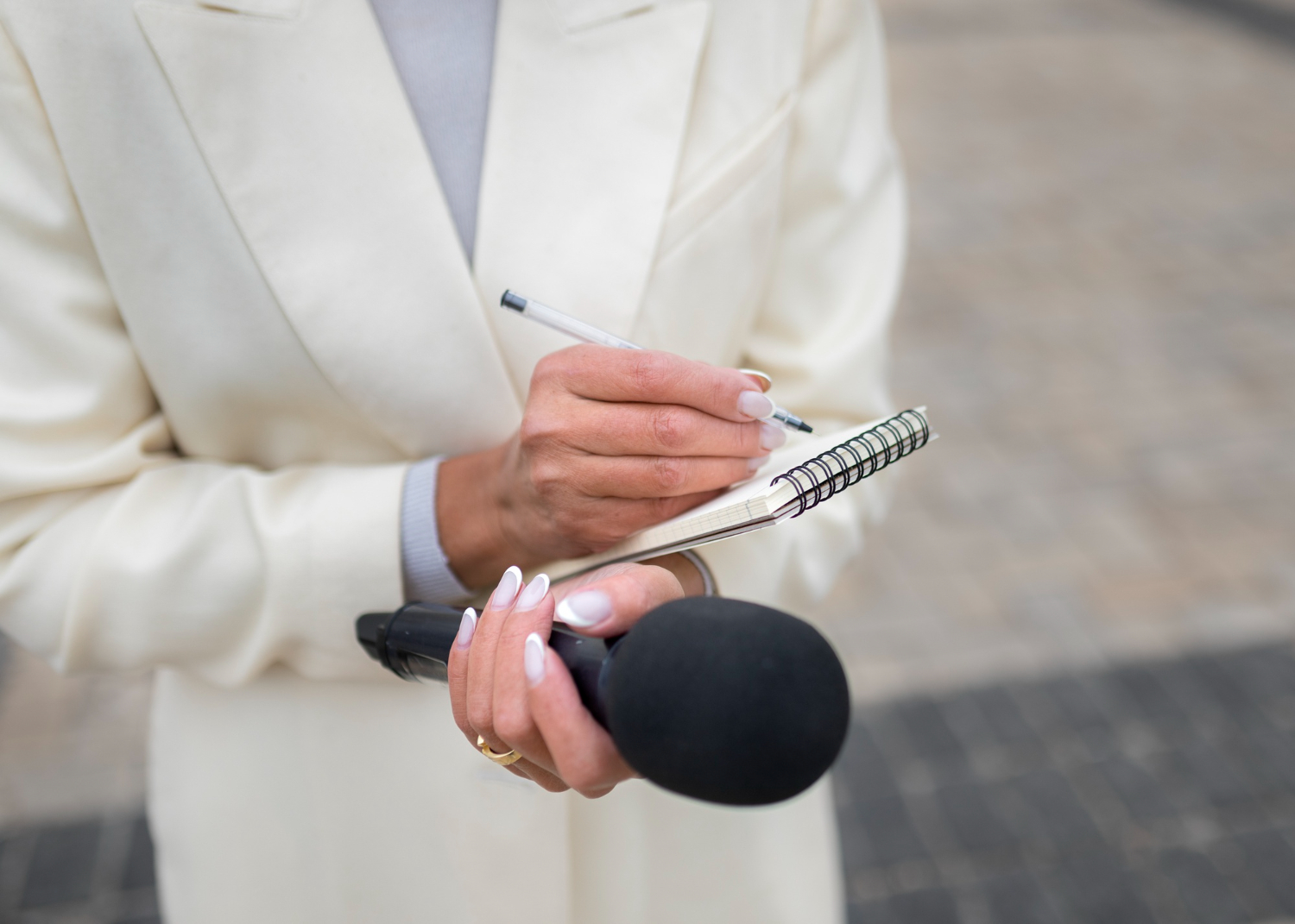 a imagem é de uma mulher fazendo anotações em um bloco e segurando um microfone, representando uma assessoria de imprensa. Seu rosto não aparece na imagem, somente do pescoço para baixo.
