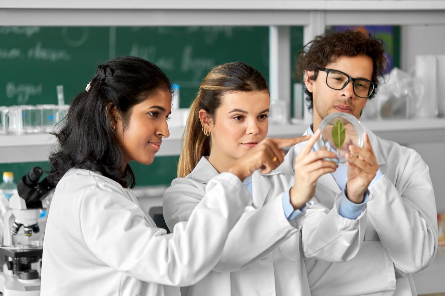 três jovens adultos em laboratório observando uma planta. todos estão com jaleco de biologos