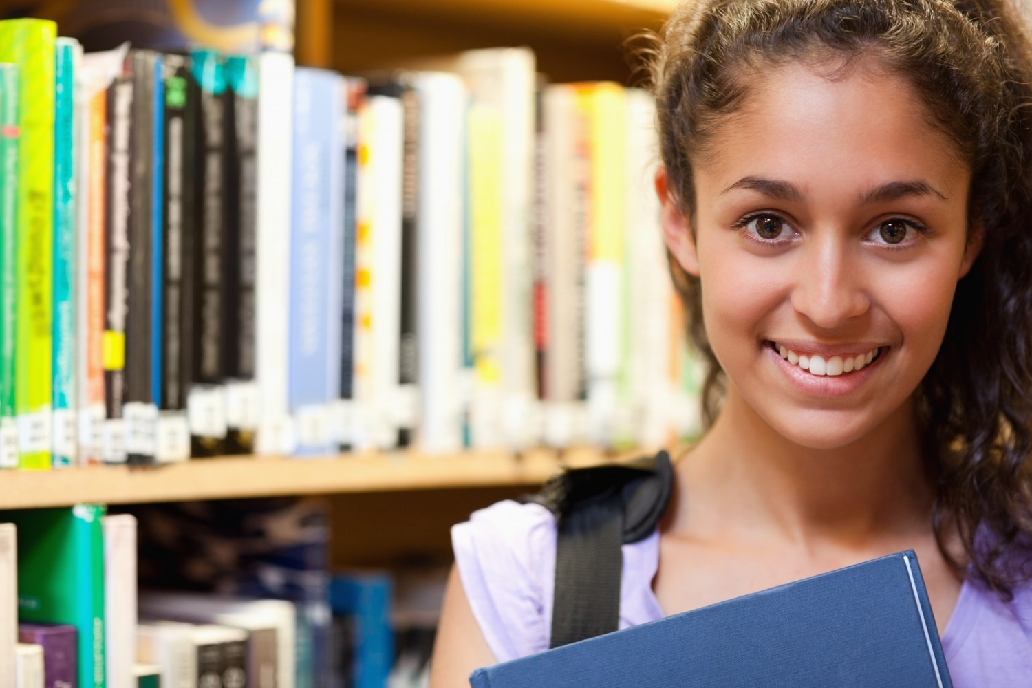 Faculdade sem TCC: imagem aproximada de uma estudante sorridente em uma biblioteca de faculdade