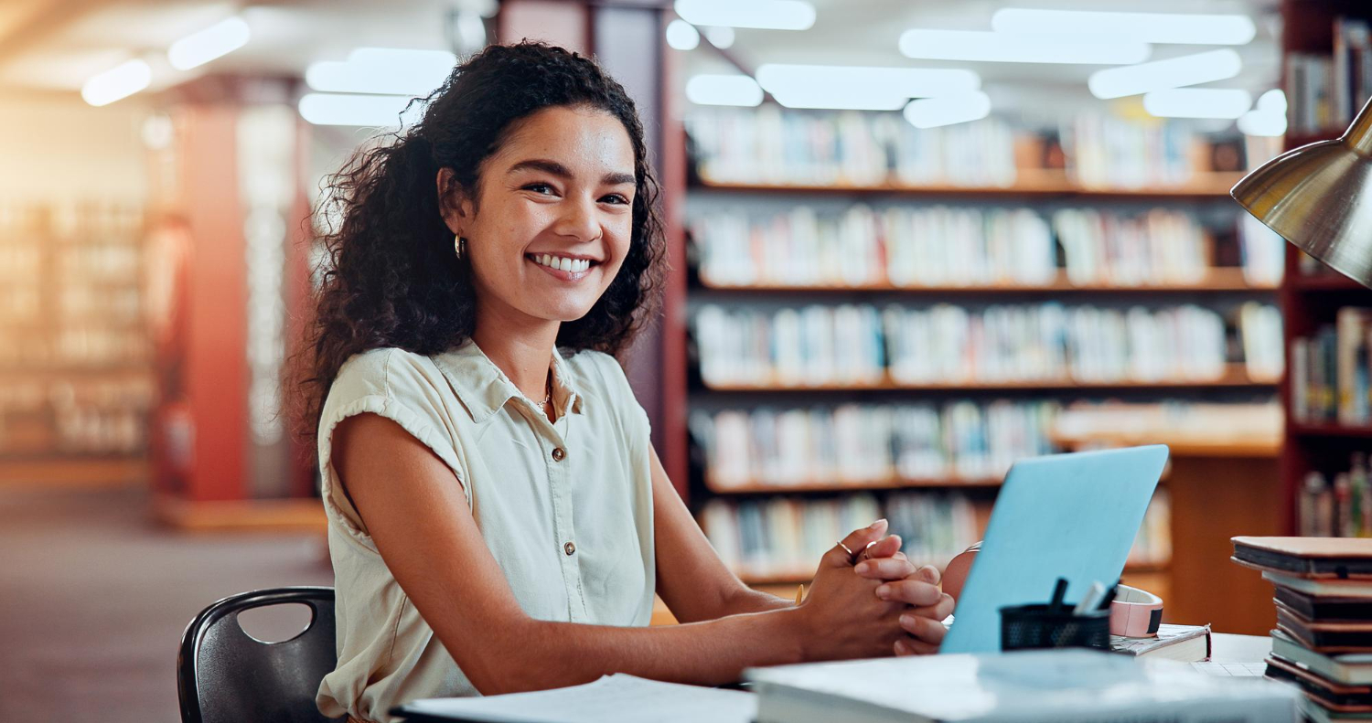 Formação acadêmica x profissional: jovem estudante em uma biblioteca, de frente para um notebook, pensando sobre seu futuro