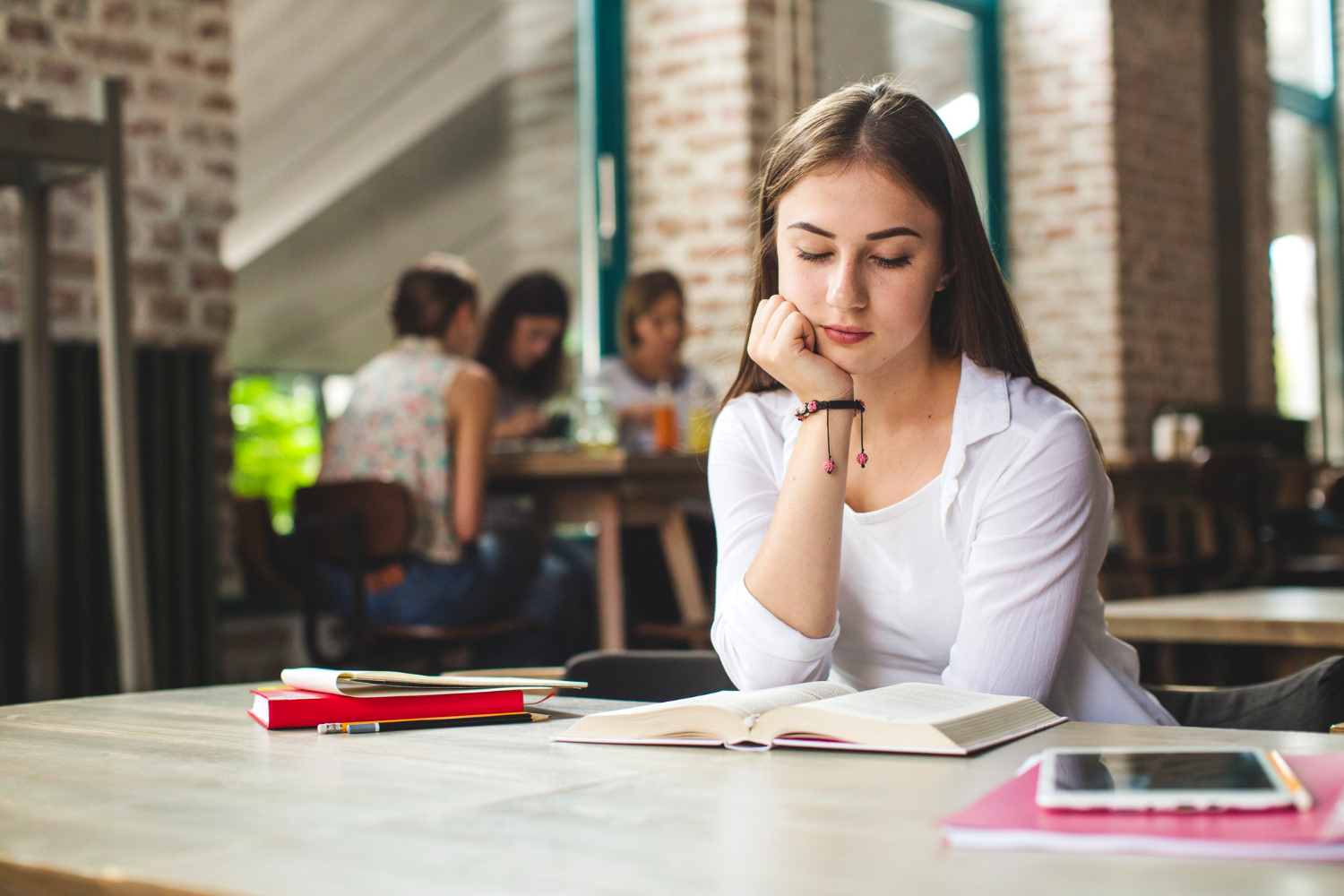 jovem adulta sentada lendo um livro aberto sobre a mesa, com expressão de concentração