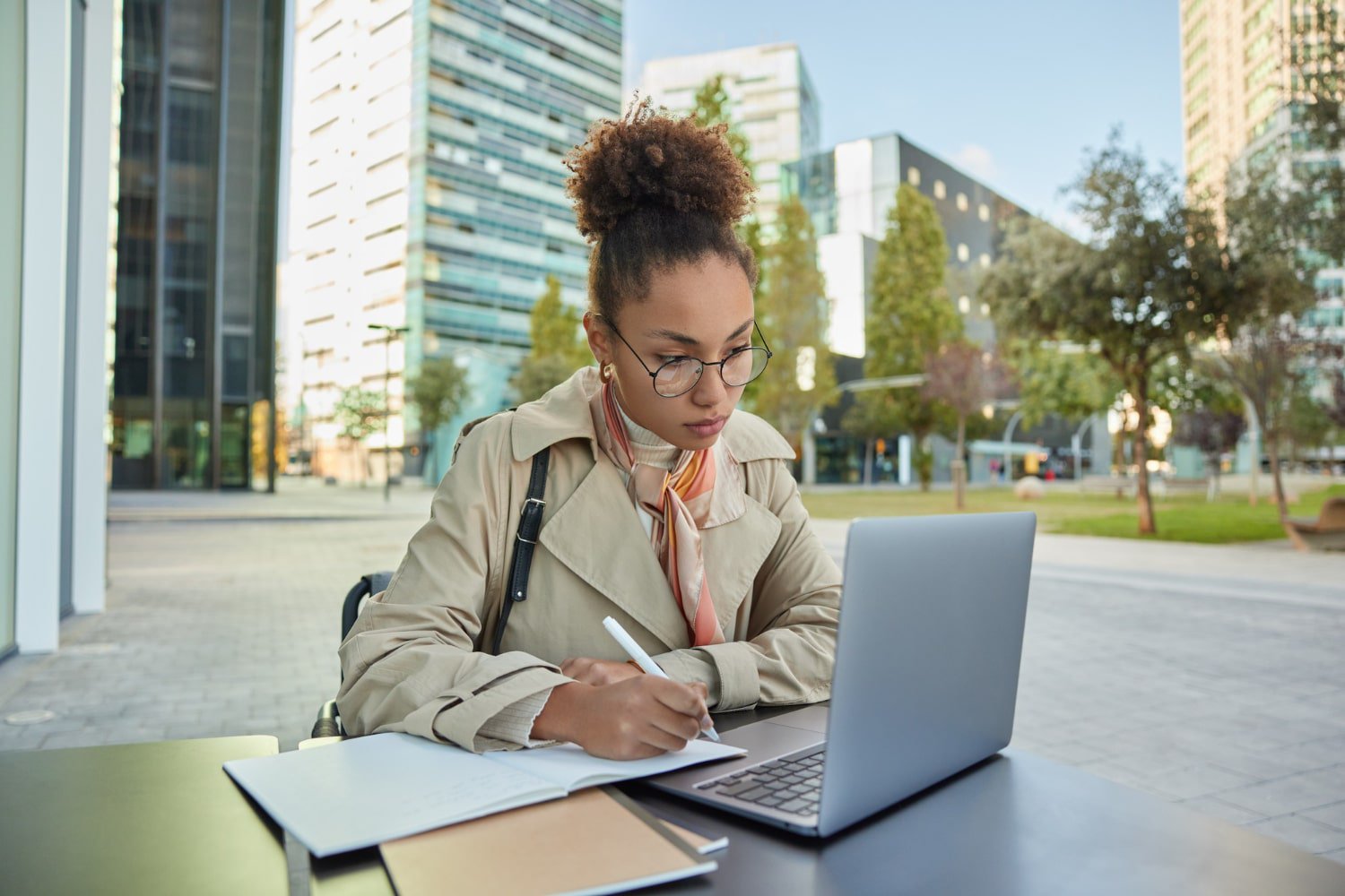 jovem adulta estudando na área externa da faculdade, com notebook e cadernos sobre uma mesa